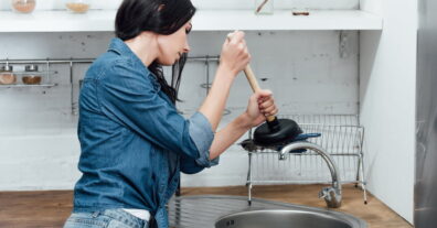 Woman using a plunger to unclog a kitchen sink drain